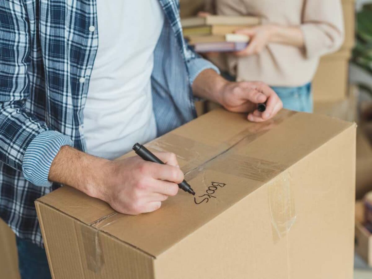 A imagem mostra uma pessoa etiquetando caixas para organizar sua mudança.